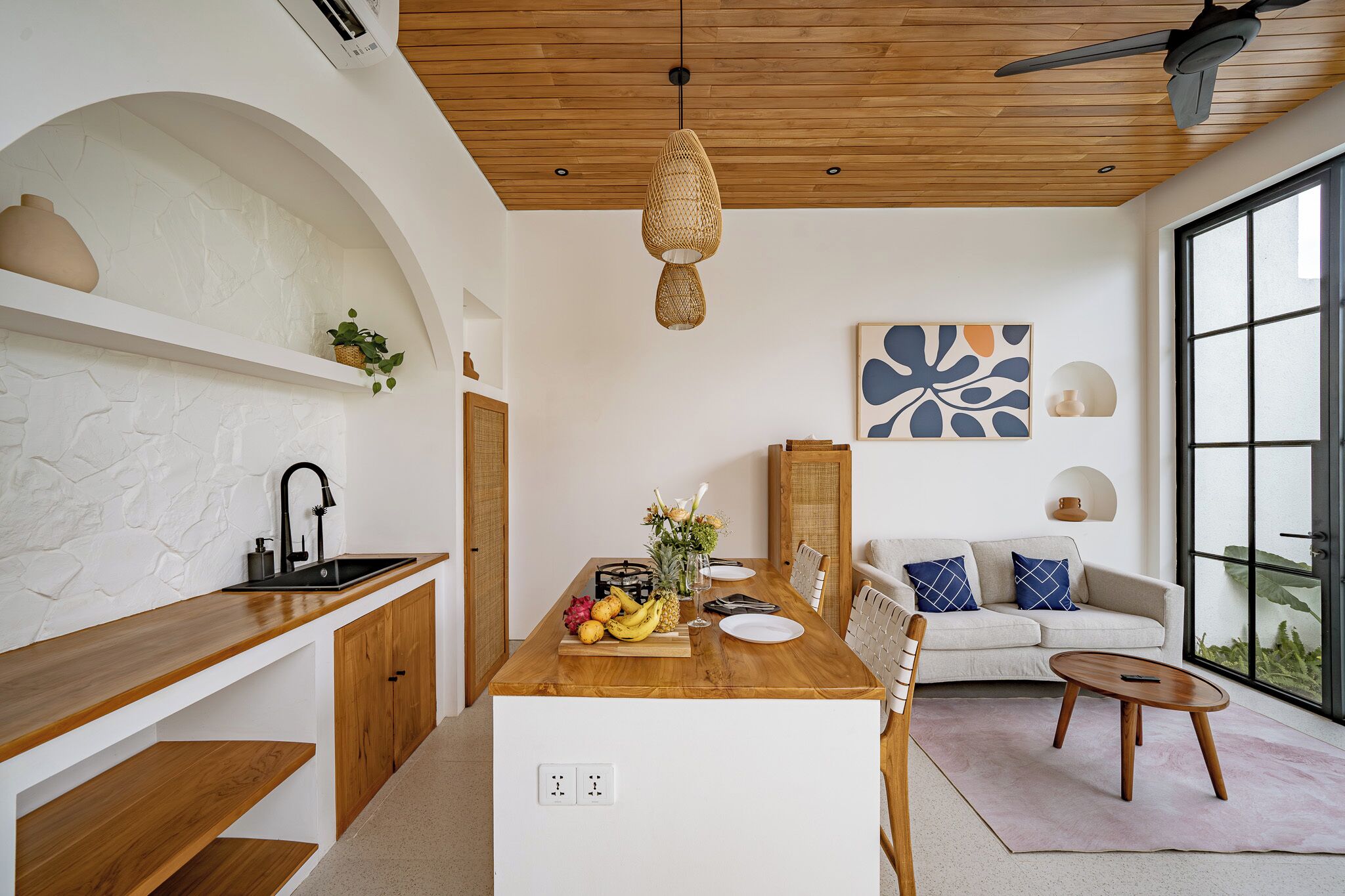 Eine moderne Küche mit einer Holzauskładung, weißen Schränken und einer zentralen Kochinsel. Es gibt einen Essbereich mit einem weißen Sofa und einem Couchtisch.