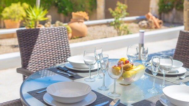 Un área de comedor al aire libre con una mesa redonda dispuesta para cuatro personas, rodeada de sillas de mimbre.