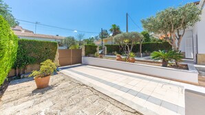 Un patio con suelo de baldosas, plantas en macetas y una pared blanca.
