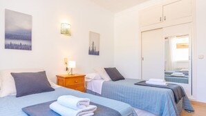 Habitación de hotel con dos camas, una mesita de noche de madera, una lámpara de pared y un espejo que refleja la habitación.