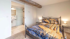 Une chambre à coucher avec un lit, des tables de chevet et une salle de bain visible à travers une porte ouverte.