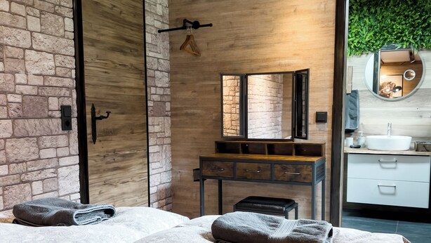 Una camera da letto moderna con un letto grande, una cassettiera in legno, uno specchio e una parete in pietra.