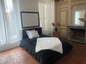 A bedroom with a bed, a nightstand, a fireplace, and a window with curtains.
