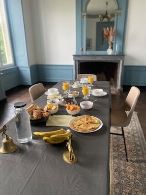 Ein Esstisch ist reichhaltig mit Frühstücksleckereien gedeckt, darunter Gebäck, Obst und eine Wasserflasche.