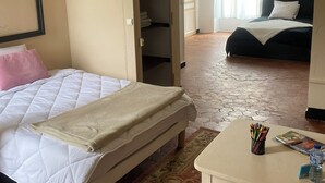 A bedroom with a bed, a bedside table with a magazine and a water bottle, a wardrobe, and a view of another room with a bed. - Bed and breakfast in a small chateau in the Loire Valley (Saint-Cyr-en-Pail)