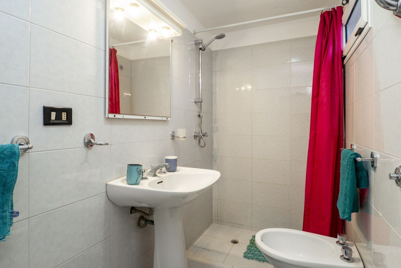 A bathroom with a sink, mirror, shower, and a red curtain.
