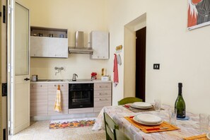 A compact kitchen with a stove, oven, and cabinets, a dining table set with plates and glasses, and a bottle of wine on the table.