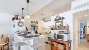 A compact kitchen with a central island, bar stools, and a microwave on a wooden stand. - Apartamento 23 Edificio Canopus - Apartment (Port D'alcúdia, Illes Balears)