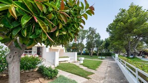 A pathway leading to a white building with a porch, surrounded by well-maintained grass and trees. - Apartamento 23 Edificio Canopus - Apartment (Port D'alcúdia, Illes Balears)