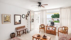 A spacious living room with a ceiling fan, wooden furniture, a television, and a view of the outdoors. - Apartamento 23 Edificio Canopus - Apartment (Port D'alcúdia, Illes Balears)