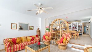 A living room with a striped sofa, wicker chairs, a glass coffee table, and a ceiling fan.
