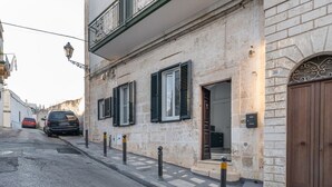 Un vicolo stretto con un edificio che presenta un balcone, un portone con una targa con il numero civico e un'auto parcheggiata.