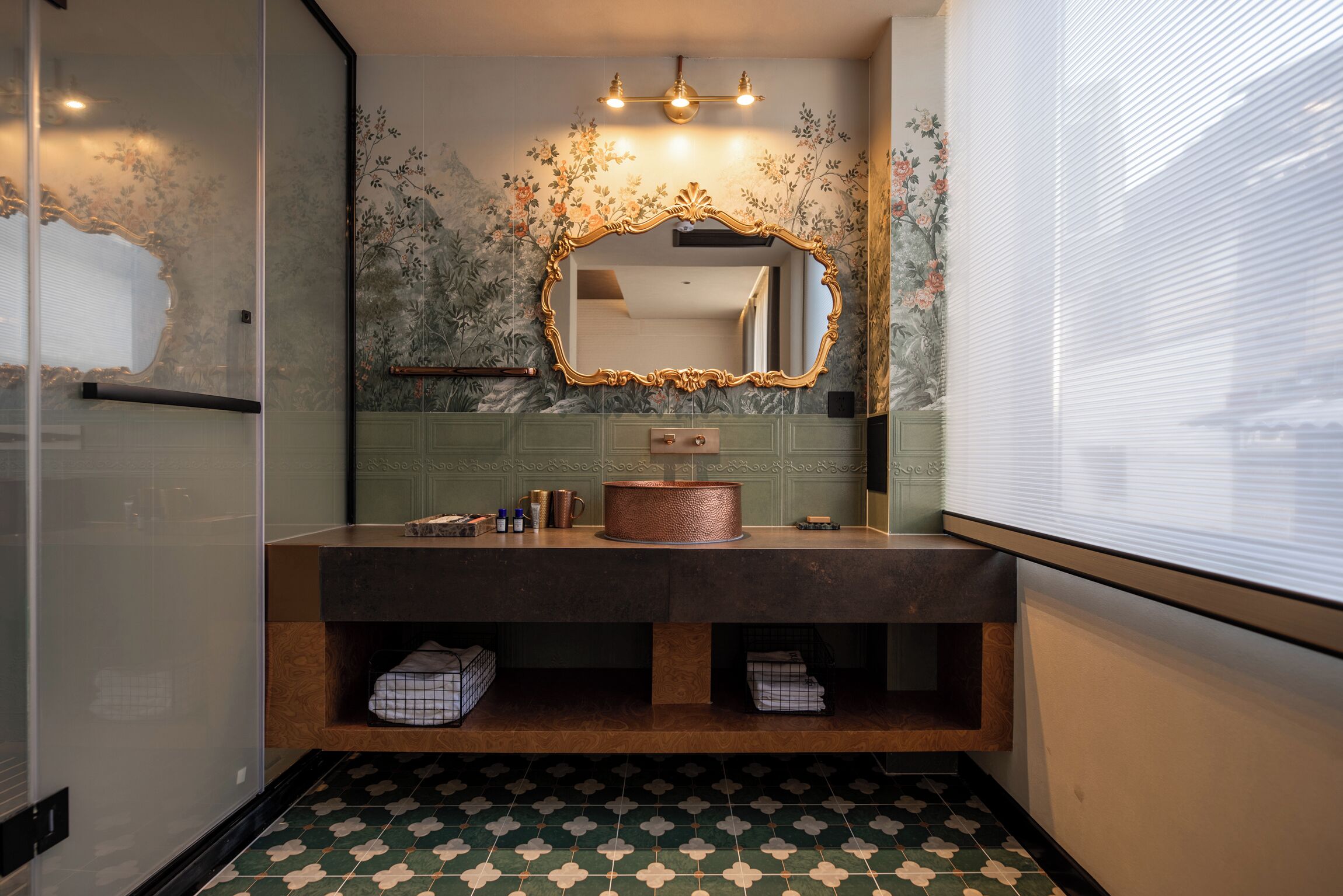 Un baño con un espejo grande, un lavamanos de cobre y un piso con diseño.