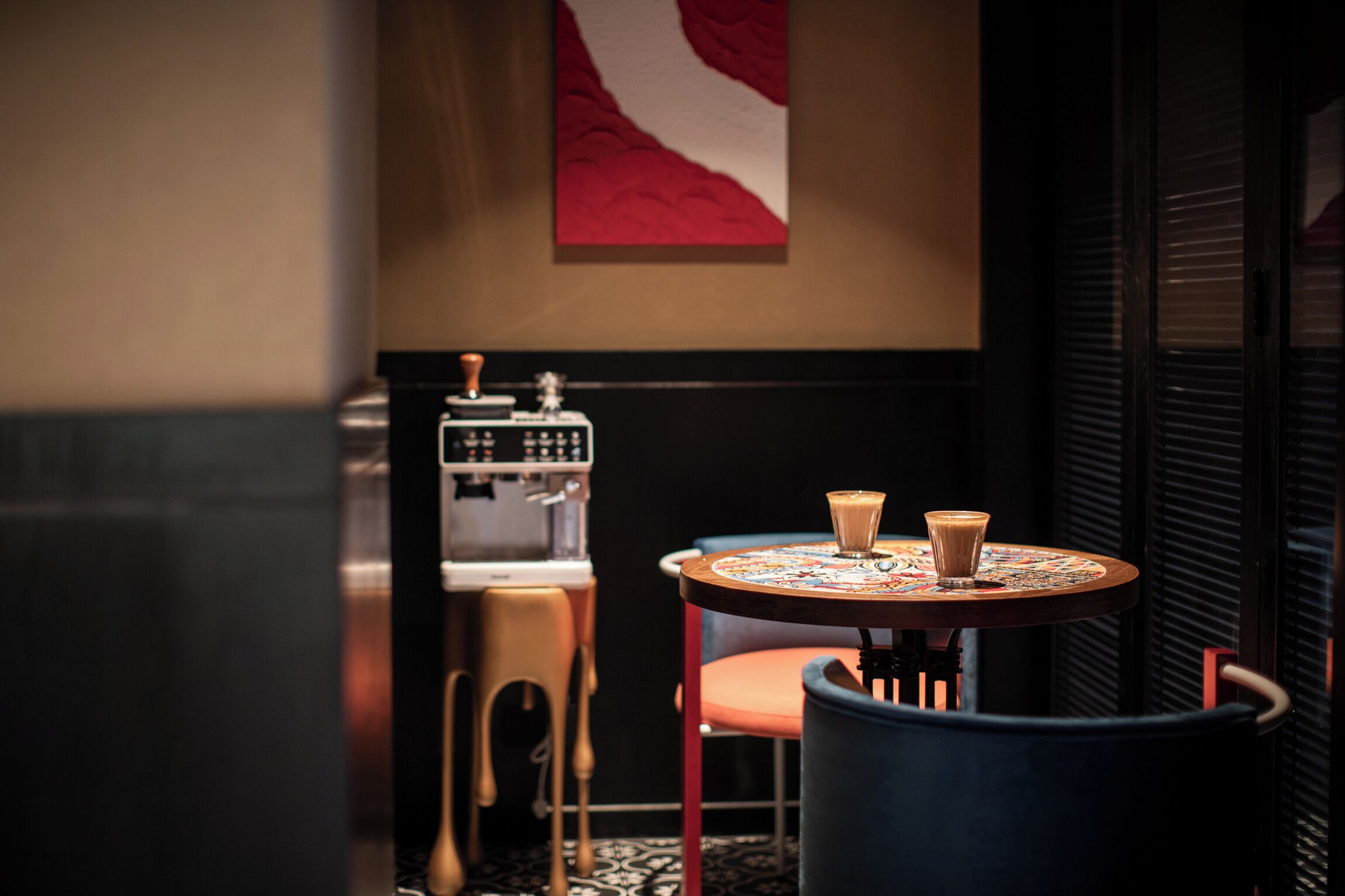 Ein gemütlicher Winkel mit einem runden Tisch, zwei Stühlen, einer Kaffeemaschine und einer wandmontierten Espressomaschine.