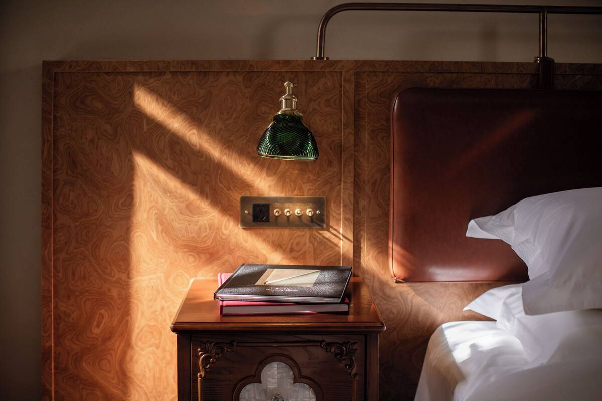 Uma cabeceira de madeira com uma luminária pendente verde, uma mesa de cabeceira com um livro e um painel de controle.