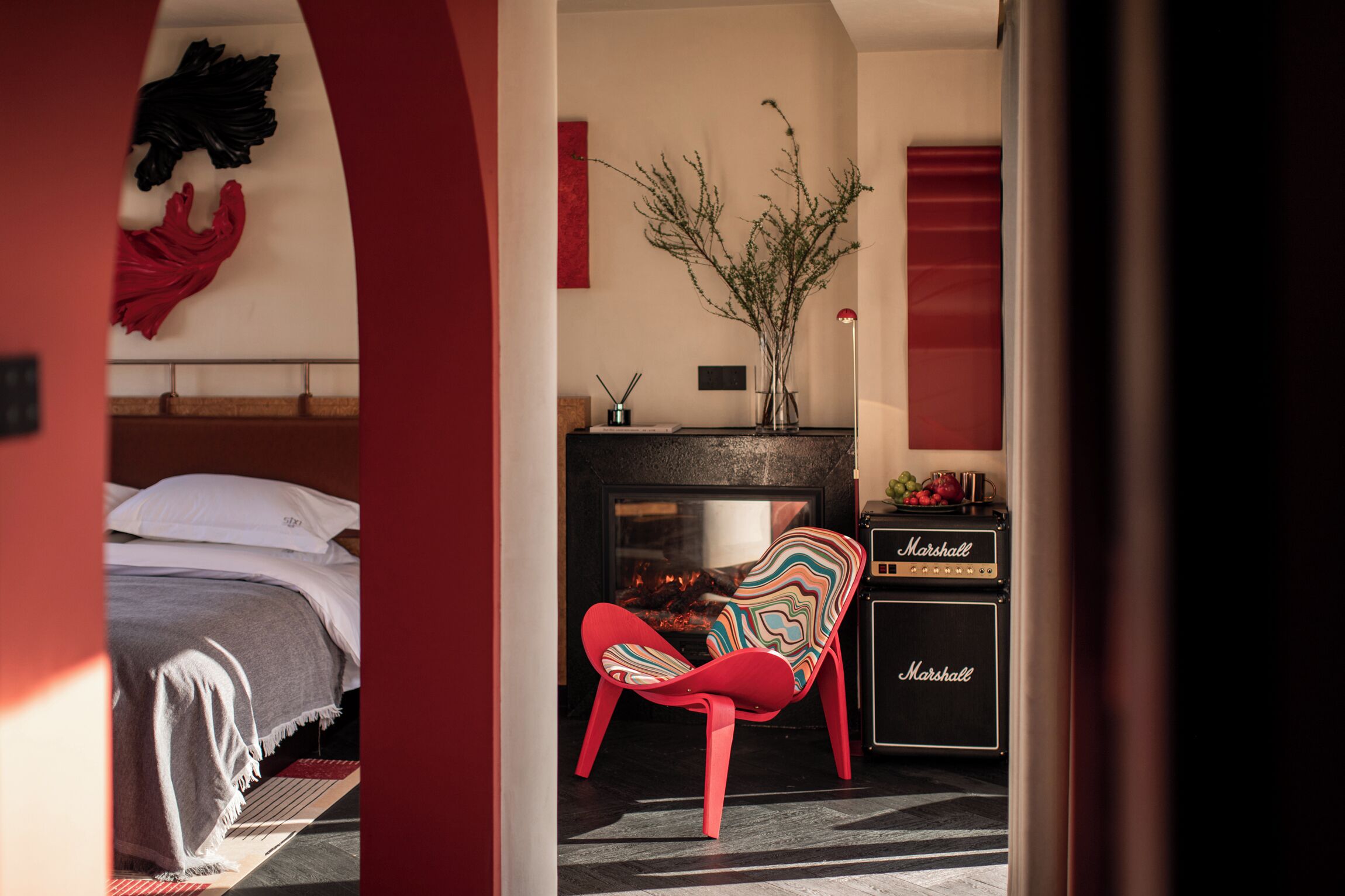 Un dormitorio con cama, una silla roja, chimenea y un amplificador Marshall.