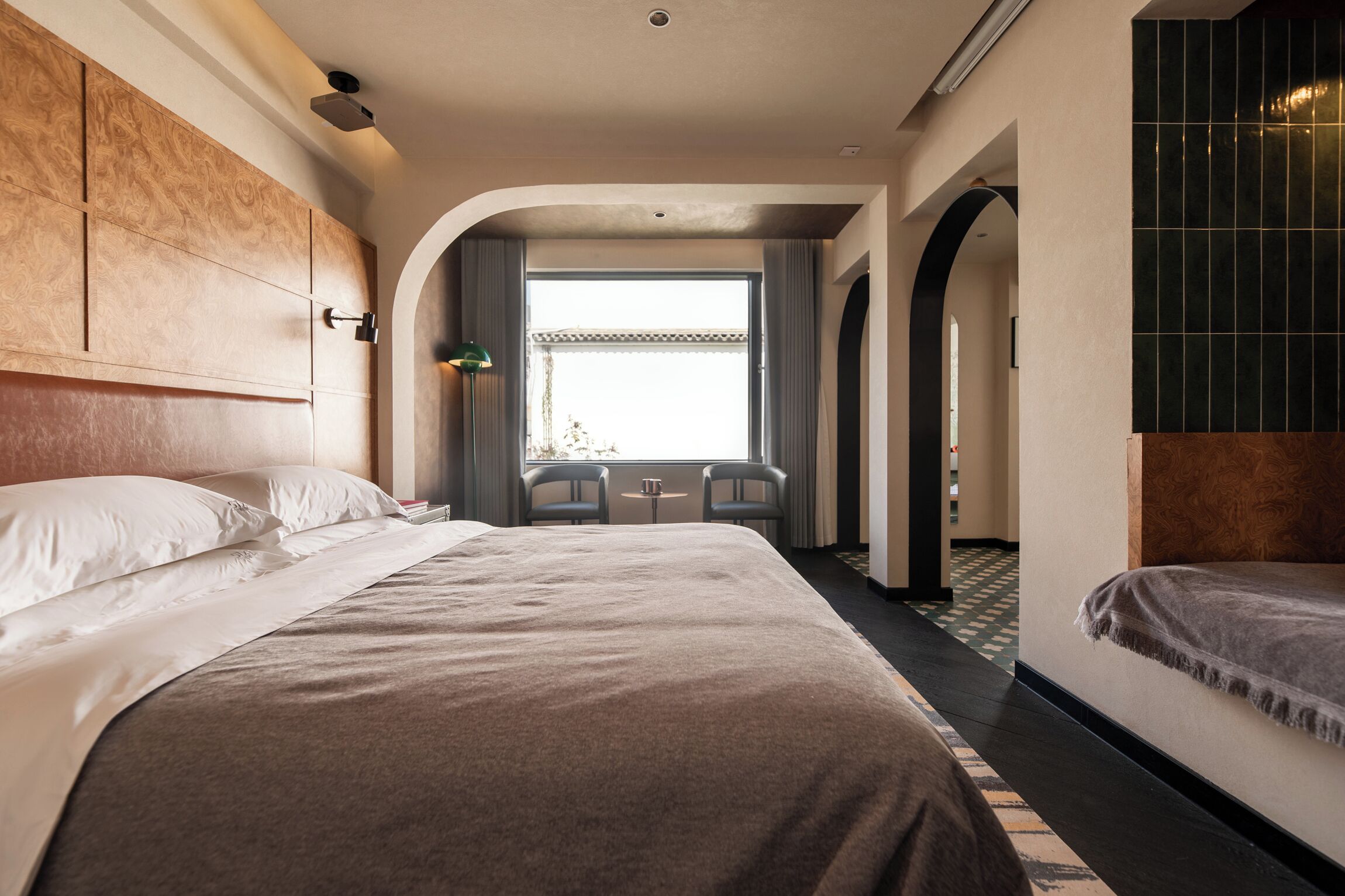 A hotel room with a large bed, a small table, two chairs, and a view of the outdoors through a window.