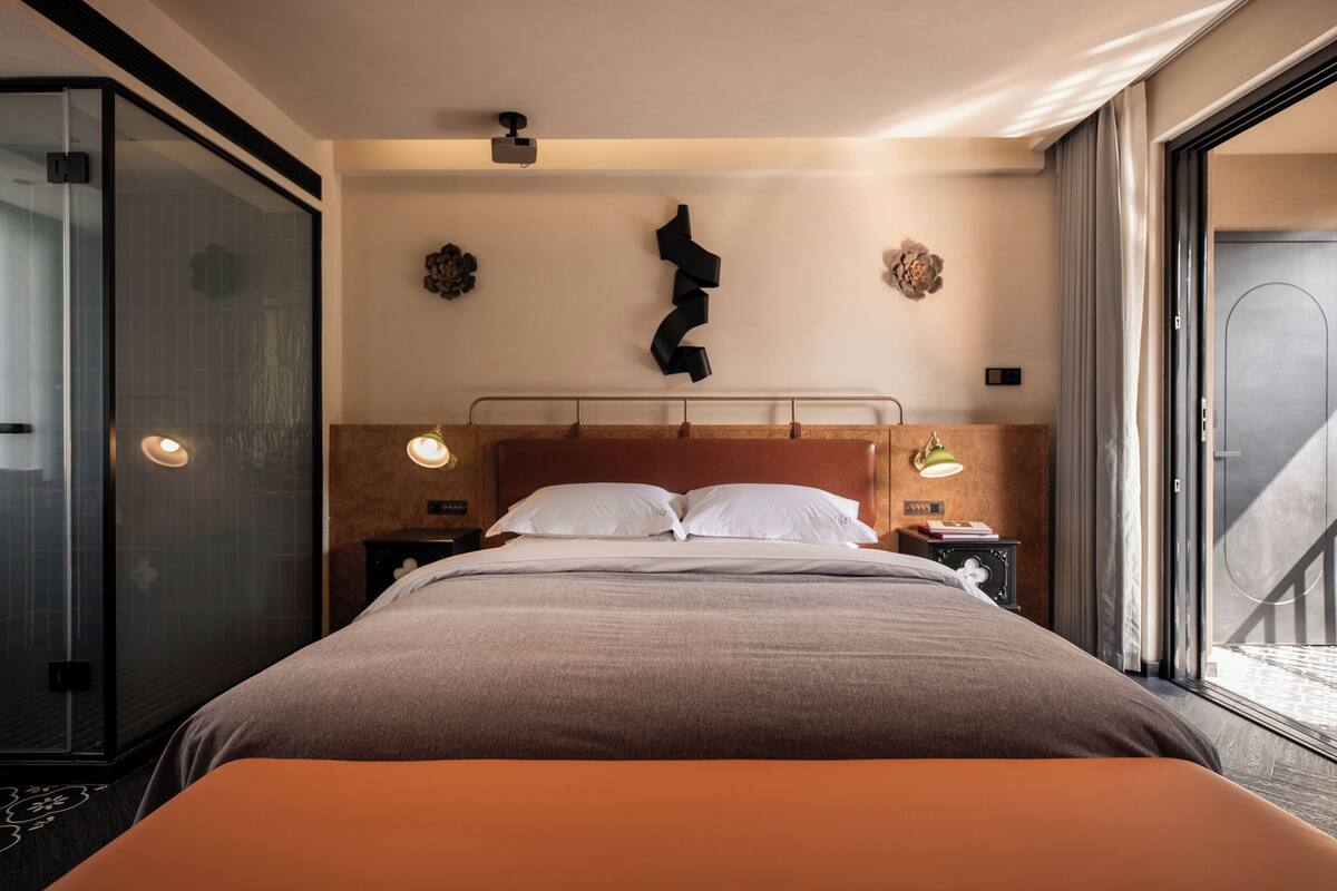 Quarto de hotel moderno com uma cama grande, box de vidro e vista para o exterior.