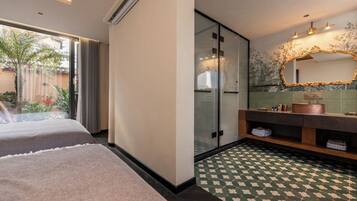 A hotel room with two beds, a glass shower enclosure, a vanity with a copper sink, and a patterned floor.