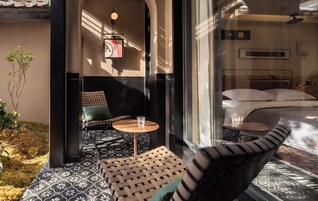 Una habitación de hotel con una cama, una mesita con un vaso y una silla con cojín.