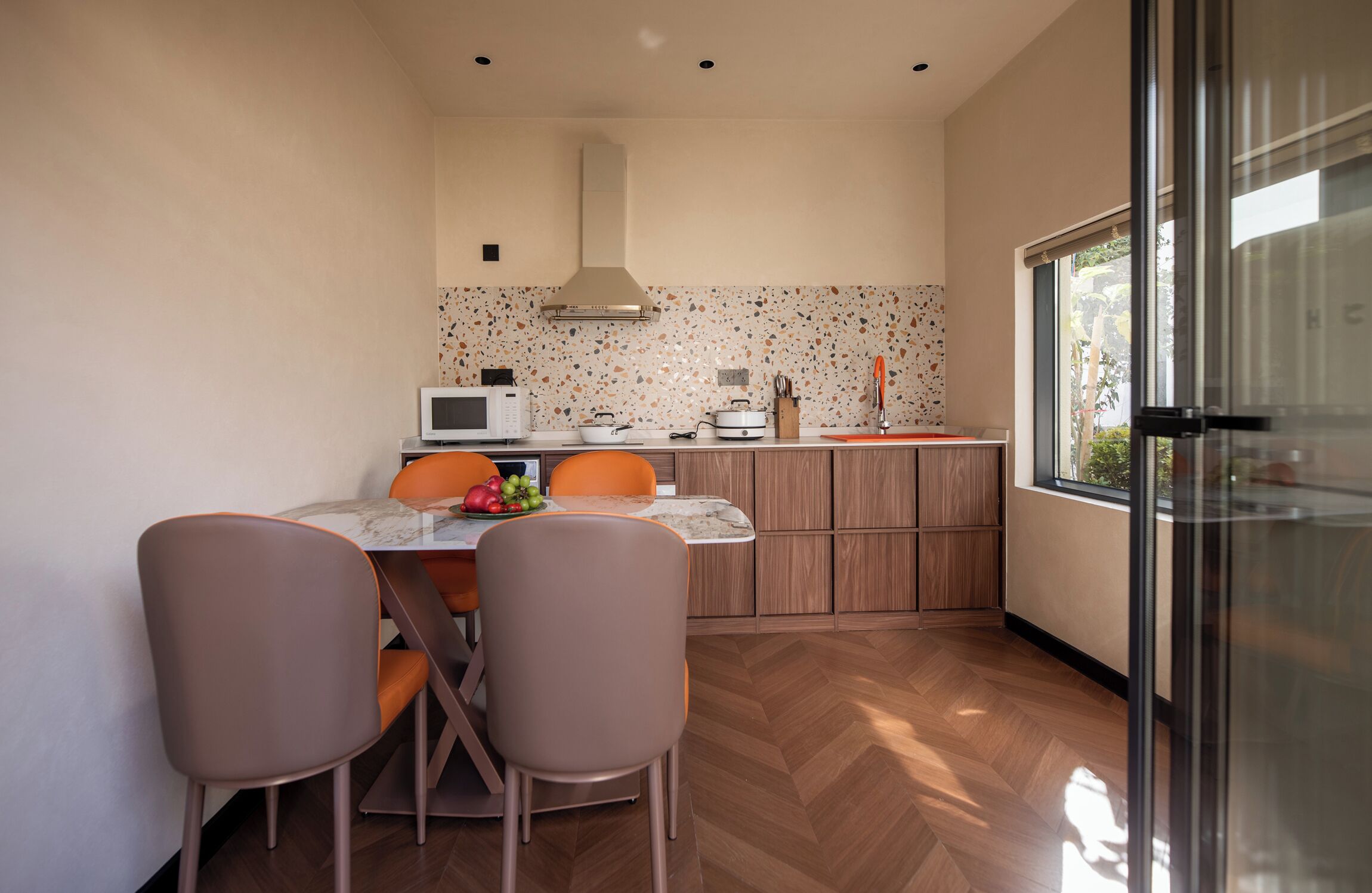Une cuisine moderne avec un coin repas, dotée d’un parquet en bois disposé en chevrons, d’une table avec un plateau en marbre et d’une grande fenêtre offrant une vue dégagée.