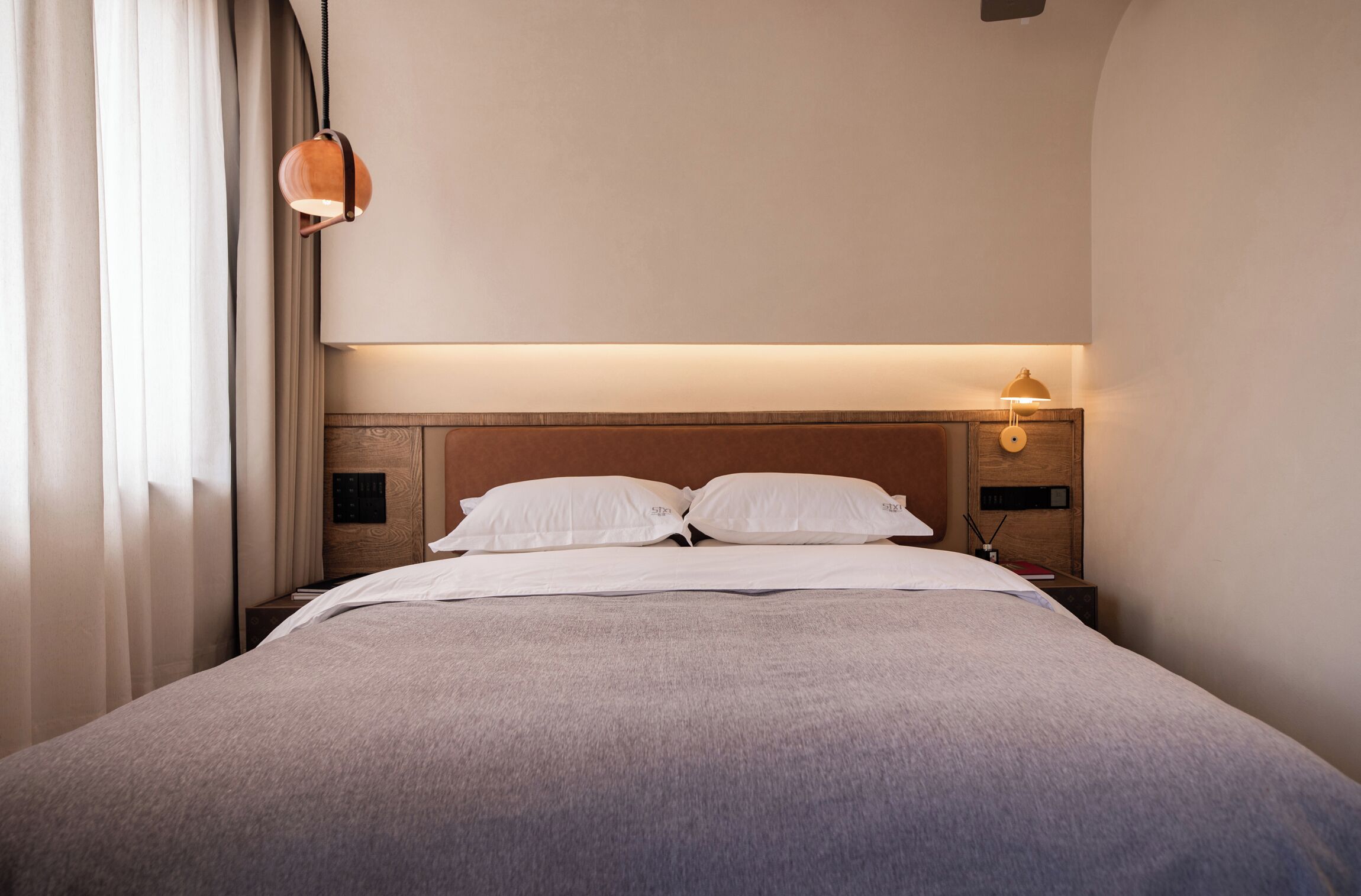 A neatly made bed with white linens, a wooden headboard, and a bedside table with a lamp.