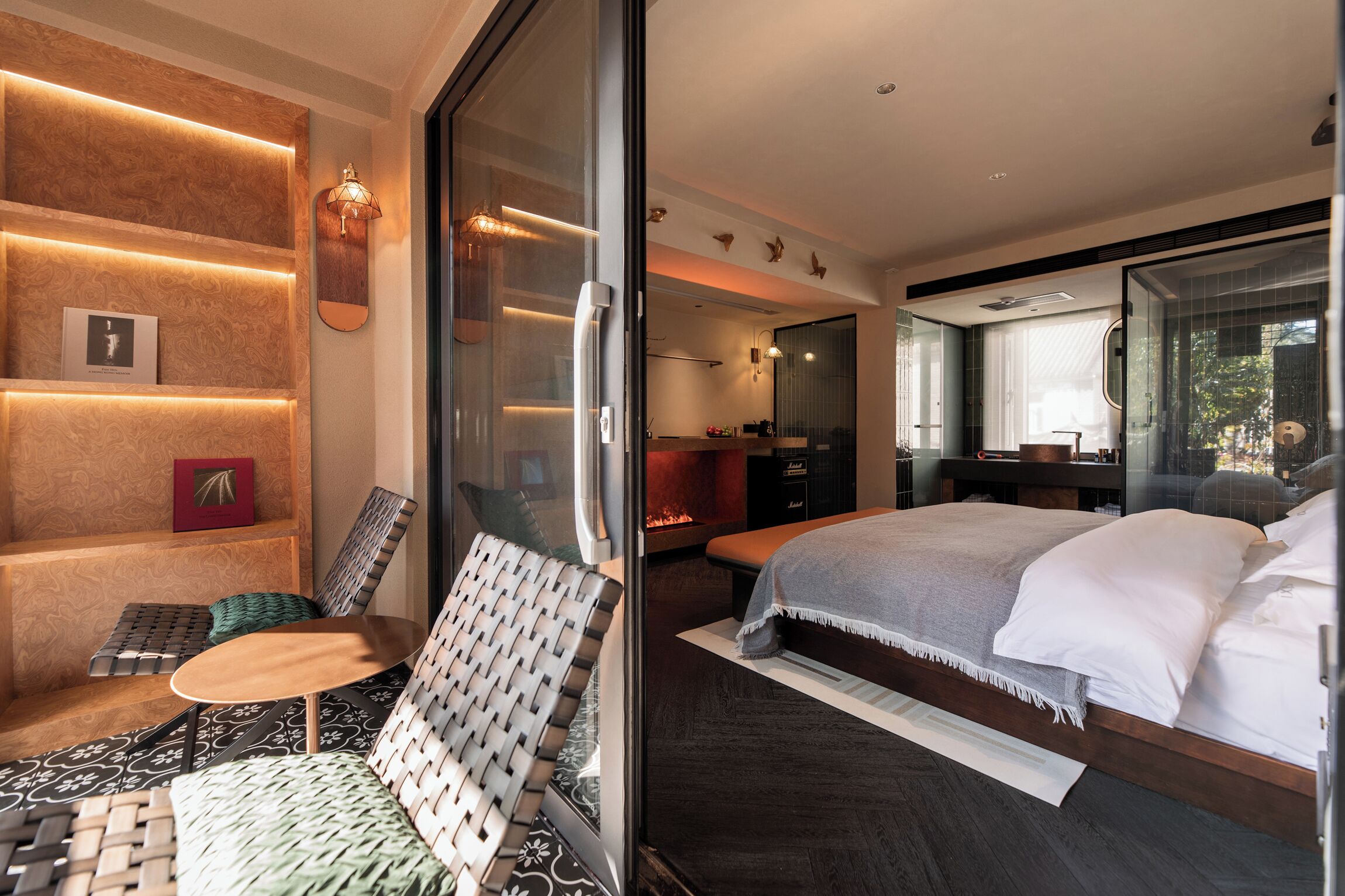 Una habitación de hotel moderna con una cama grande, una zona de estar con una silla y una mesa, una chimenea y un ventanal que da a un balcón.