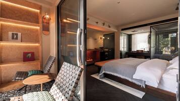 Una habitación de hotel moderna con una cama grande, una zona de estar con una silla y una mesa, una chimenea y un ventanal que da a un balcón.