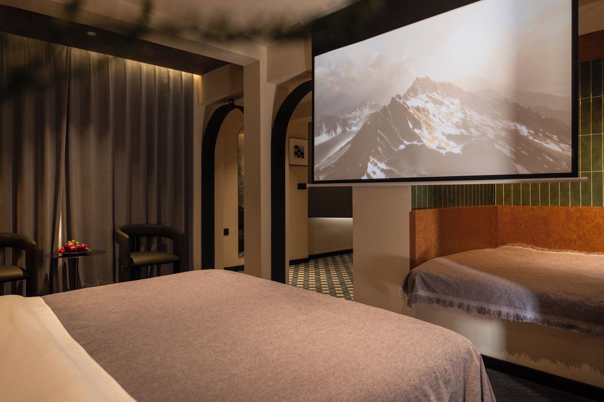 A hotel room with two beds, a television mounted on the wall, a small table with fruit, and a patterned floor.