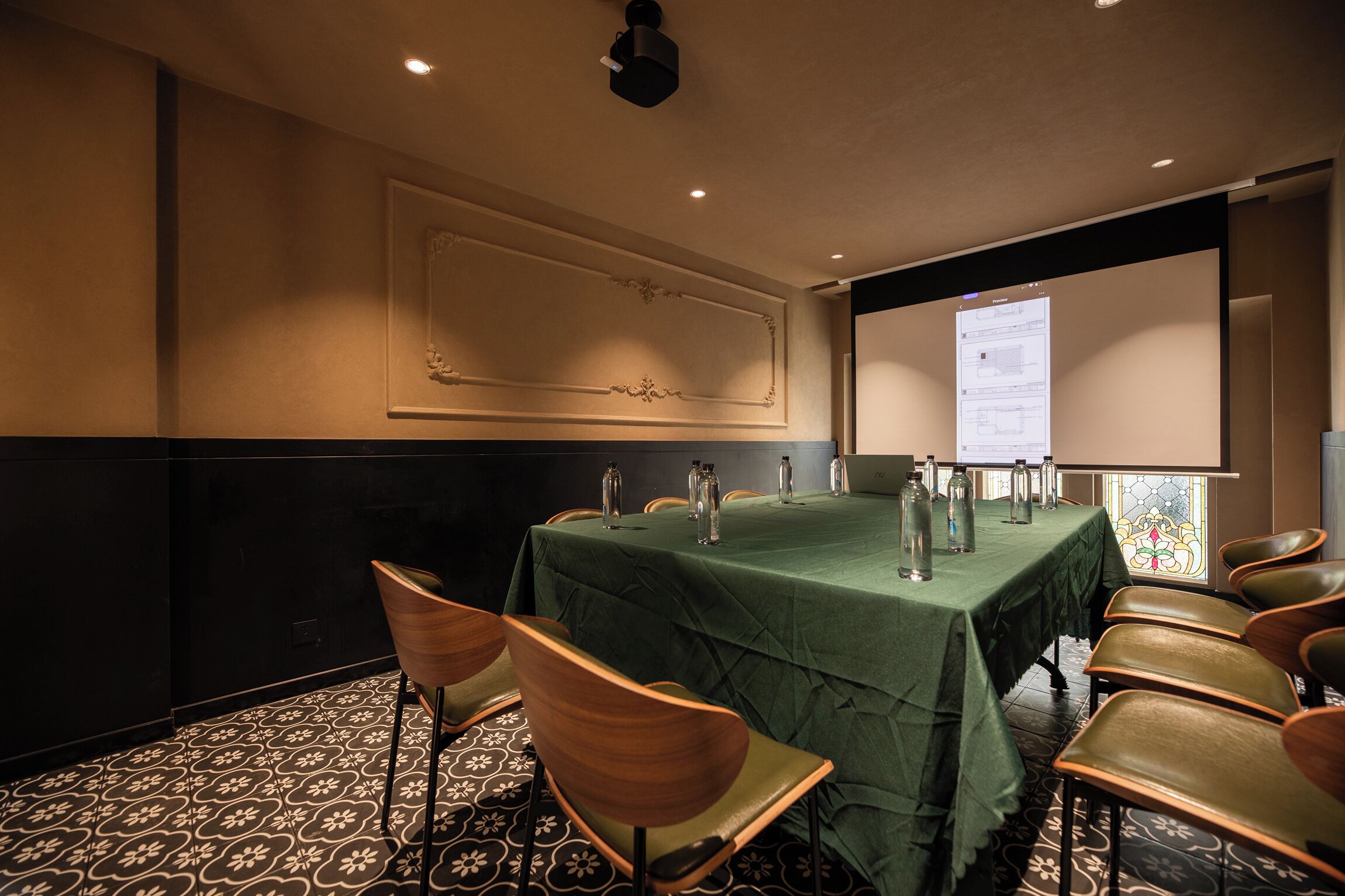 A conference room with a green table, chairs, a projector screen, and a stained glass window.