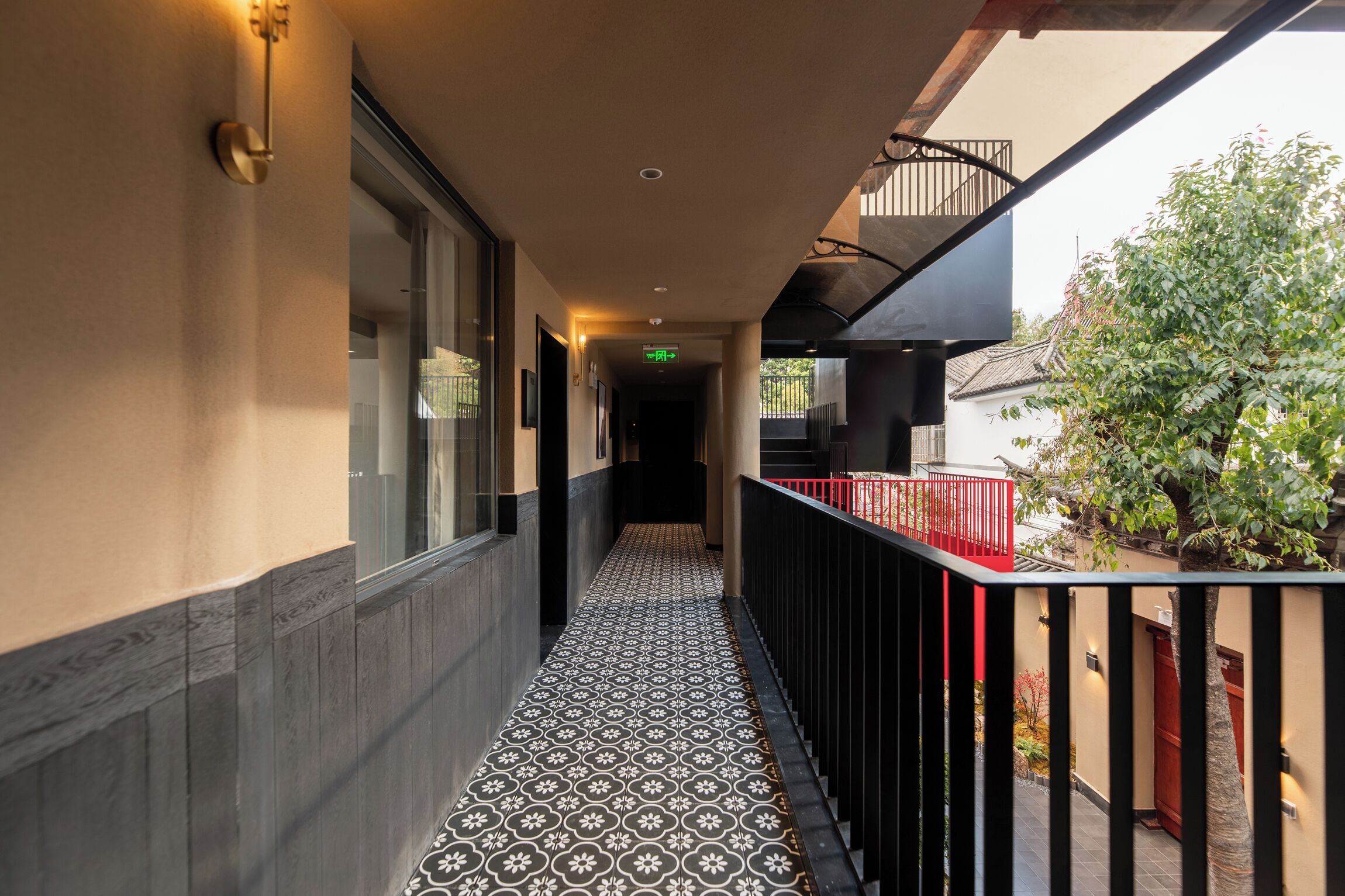 A corridor with patterned flooring, a red railing, and a view of a tree and building outside.