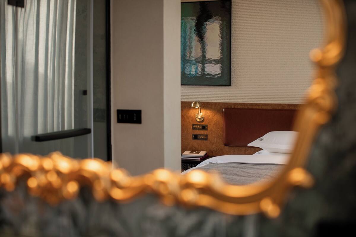 Quarto de hotel com uma cama, mesa de cabeceira, abajur e um quadro na parede.