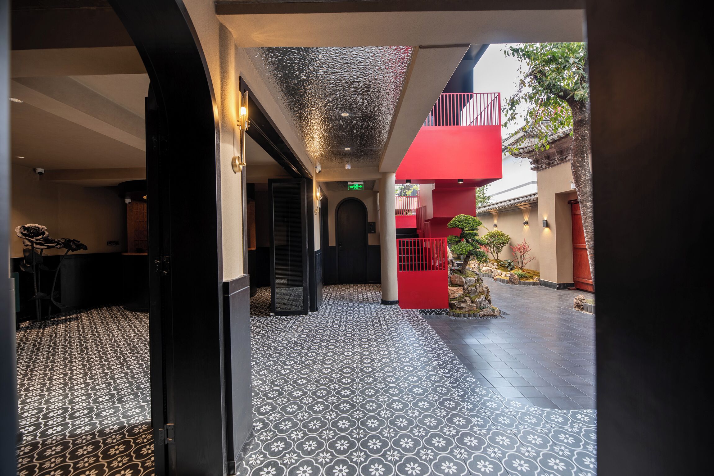 Et hotel med et mønstret gulv, en rød balkon og et lille haveområde.