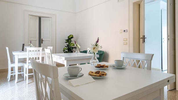 A dining area with a white table, chairs, a chandelier, and a view through an open door. - GuestHost Chic B&B Piazza Libertà - Suite Lecce (Ostuni)