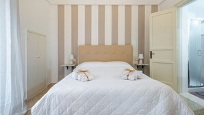 A hotel room with a large bed, striped wall, bedside tables, and a door leading to a bathroom. - GuestHost Chic B&B Piazza Libertà - Suite Lecce (Ostuni)