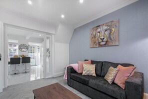 A modern living room with a grey sofa, a wooden coffee table, and a large abstract painting on the wall. - Family-Friendly 4-Bed near Parks & Transport Links (Great Barr)