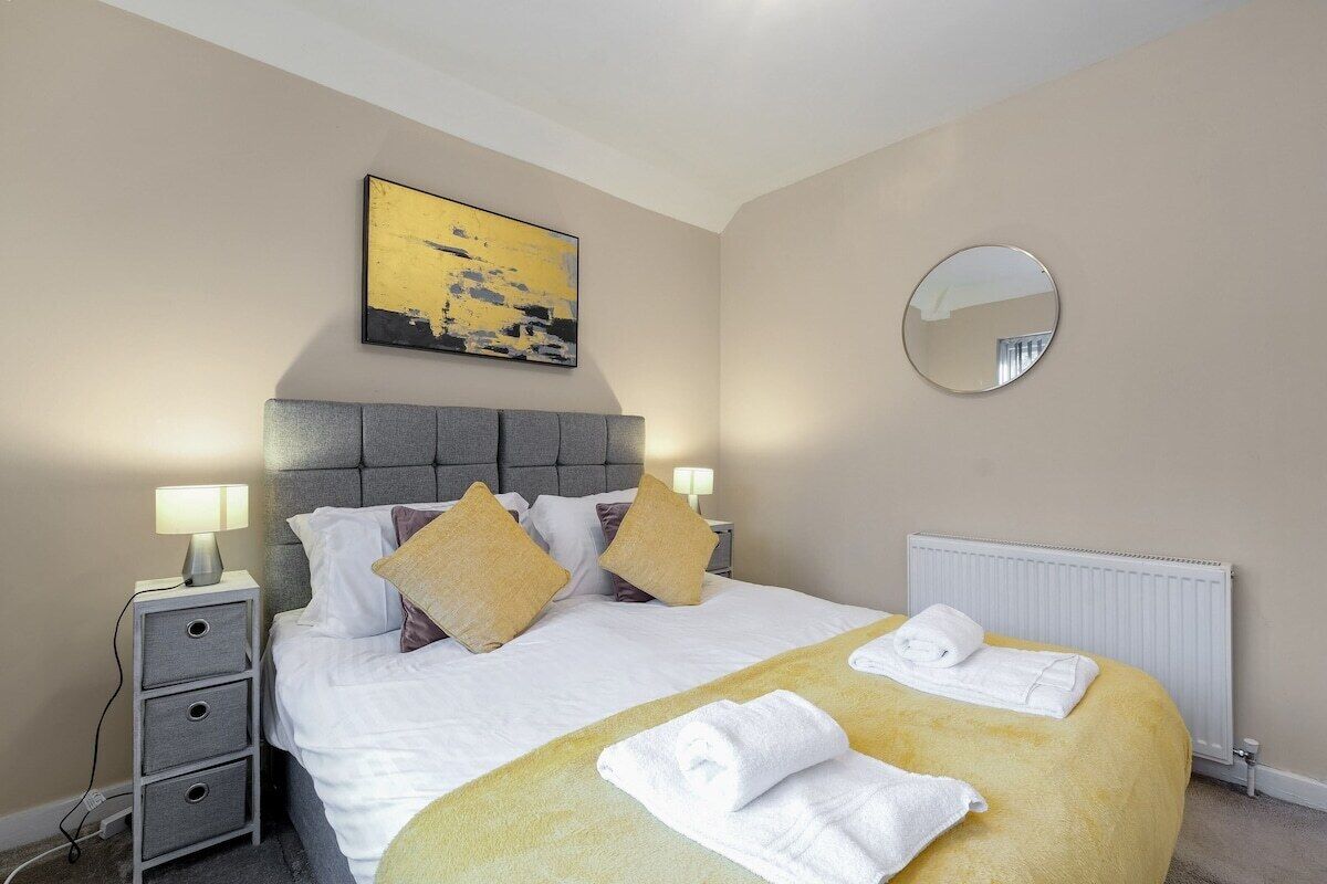 A hotel room with a bed, bedside lamps, a mirror, a radiator, and a painting on the wall.