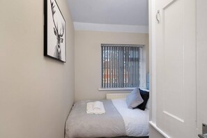 Une petite chambre avec un lit simple, une fenêtre, un radiateur et une porte.