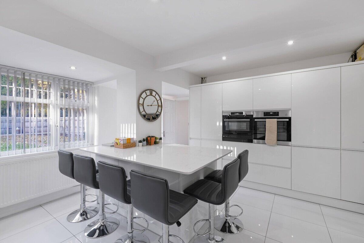 A modern kitchen with white cabinetry, a central island with bar stools, and a round wall clock.