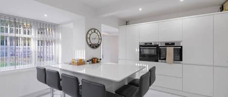 A modern kitchen with white cabinetry, a central island with bar stools, and a round wall clock.