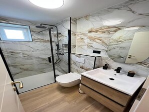 A modern bathroom with a glass shower enclosure, a white sink, and a marble-patterned wall. - Apartments Kalinić (Janjina)