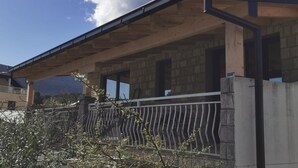 A building with a covered patio area, stone walls, and a metal railing. - Apartments Kalinić (Janjina)