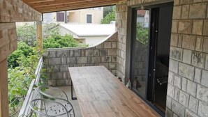 A covered outdoor area with a wooden table and chairs, stone walls, and a glass door. - Apartments Kalinić (Janjina)