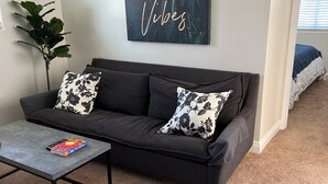 A living room with a dark grey sofa, two floral cushions, a coffee table with a book, and a wall art piece saying "Good Vibes". - Spacious 5-Master suite house in UC Riverside with individual AC, WiFi. Enjoy! (Riverside)