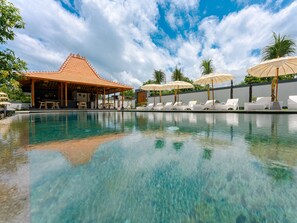 A clear swimming pool with lounge chairs and umbrellas, a covered seating area, and palm trees. - Bubu Homestay Tulamben (Tulamben)