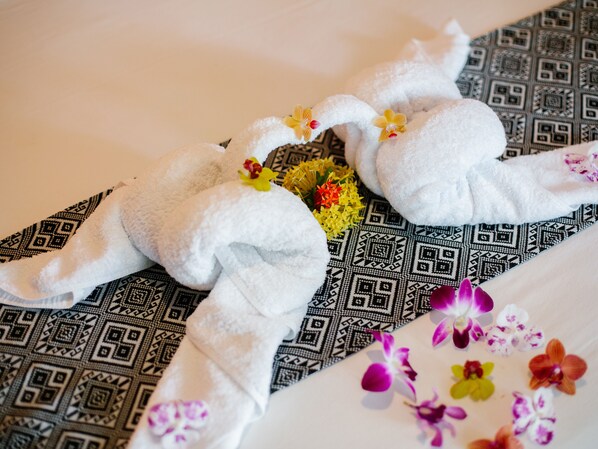 A bed with a patterned bedspread, a white towel, and a bouquet of flowers. - Bubu Homestay Tulamben (Tulamben)