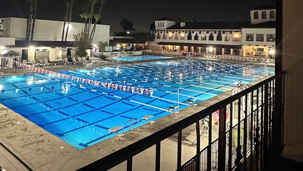 A swimming pool with lane dividers and a flag line, surrounded by a balcony with a railing. - Resort Style Home near Beaches & Disneyland (Fountain Valley)
