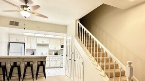 A spacious kitchen with white cabinets, a central island with bar stools, and a ceiling fan. - Resort Style Home near Beaches & Disneyland (Fountain Valley)