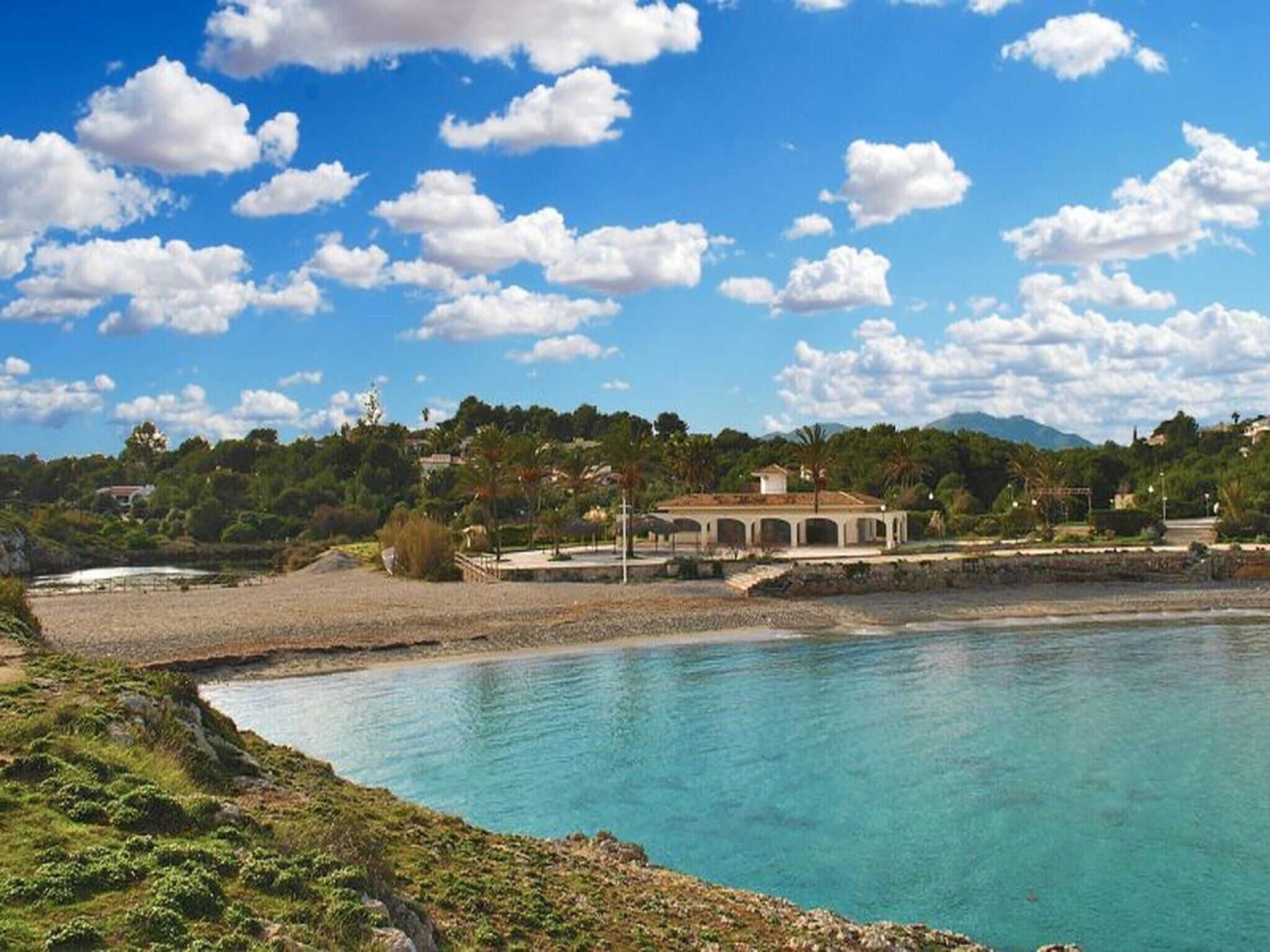 A coastal property with a large building, a beach, and a clear blue sky.