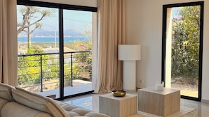 Una sala de estar moderna con un sofá grande, una mesita auxiliar y una lámpara de pie. Amplias ventanas con cortinas ofrecen vistas al exterior.